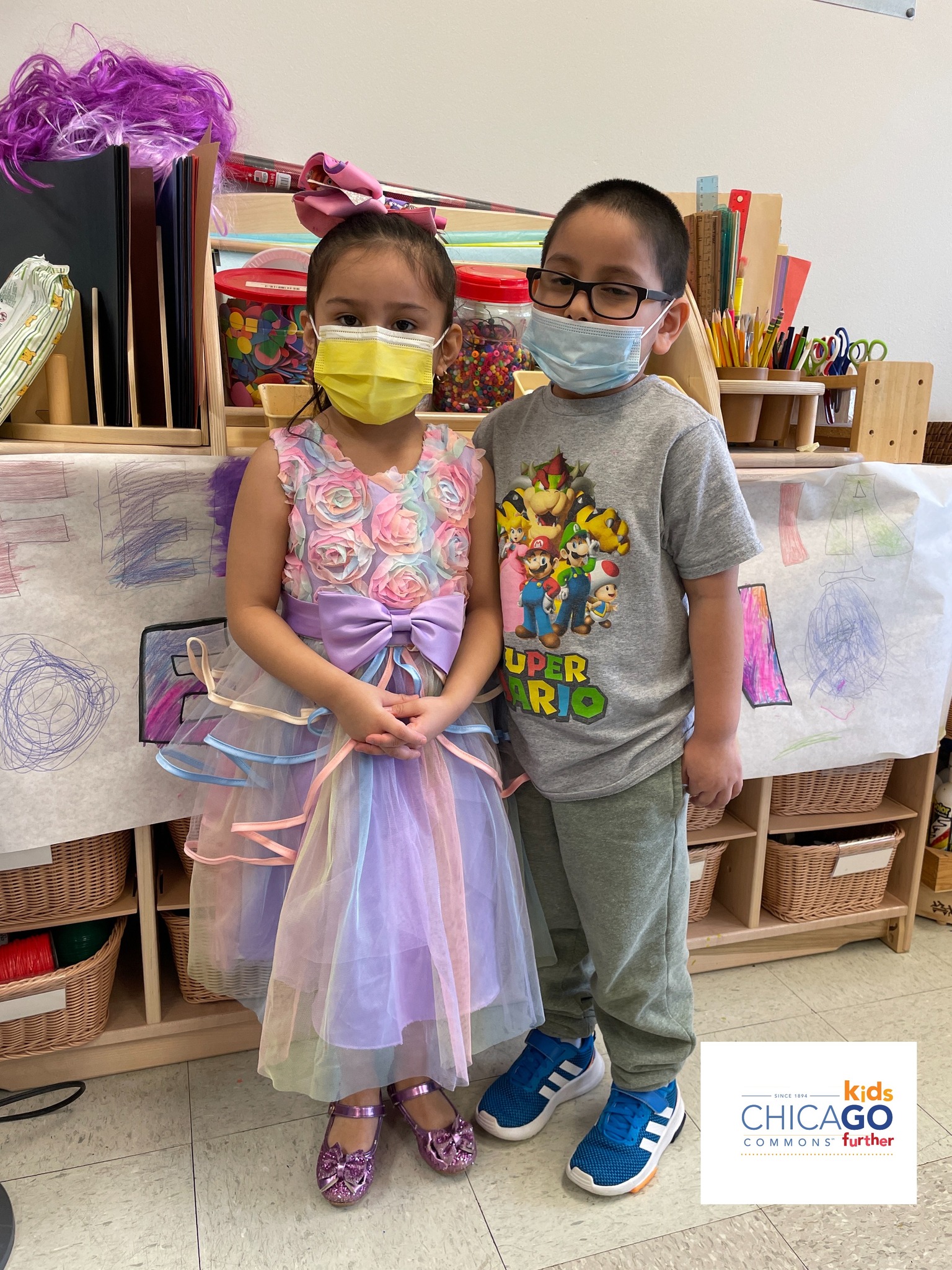 Two children celebrate Week of the Young Child 2023 by posing in front of a classroom-drawn mural.